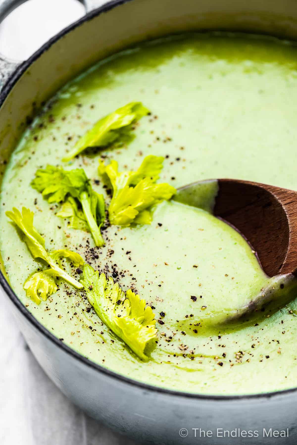 A close up of celery soup in a pot with a wooden spoon.