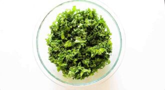 A glass bowl filled with finely chopped fresh kale, perfect for preparing a vibrant kale apple salad, on a white background.