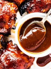A spoon scooping some bbq sauce for chicken with bbq chicken on the side.