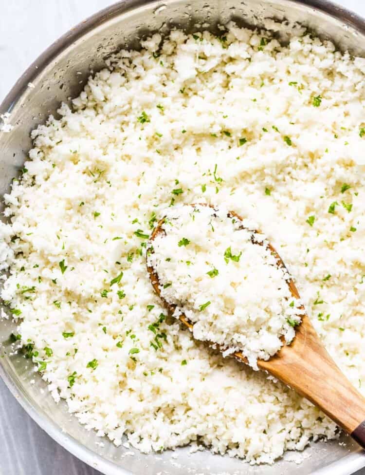 cauliflower rice in a pan with a wooden spoon.