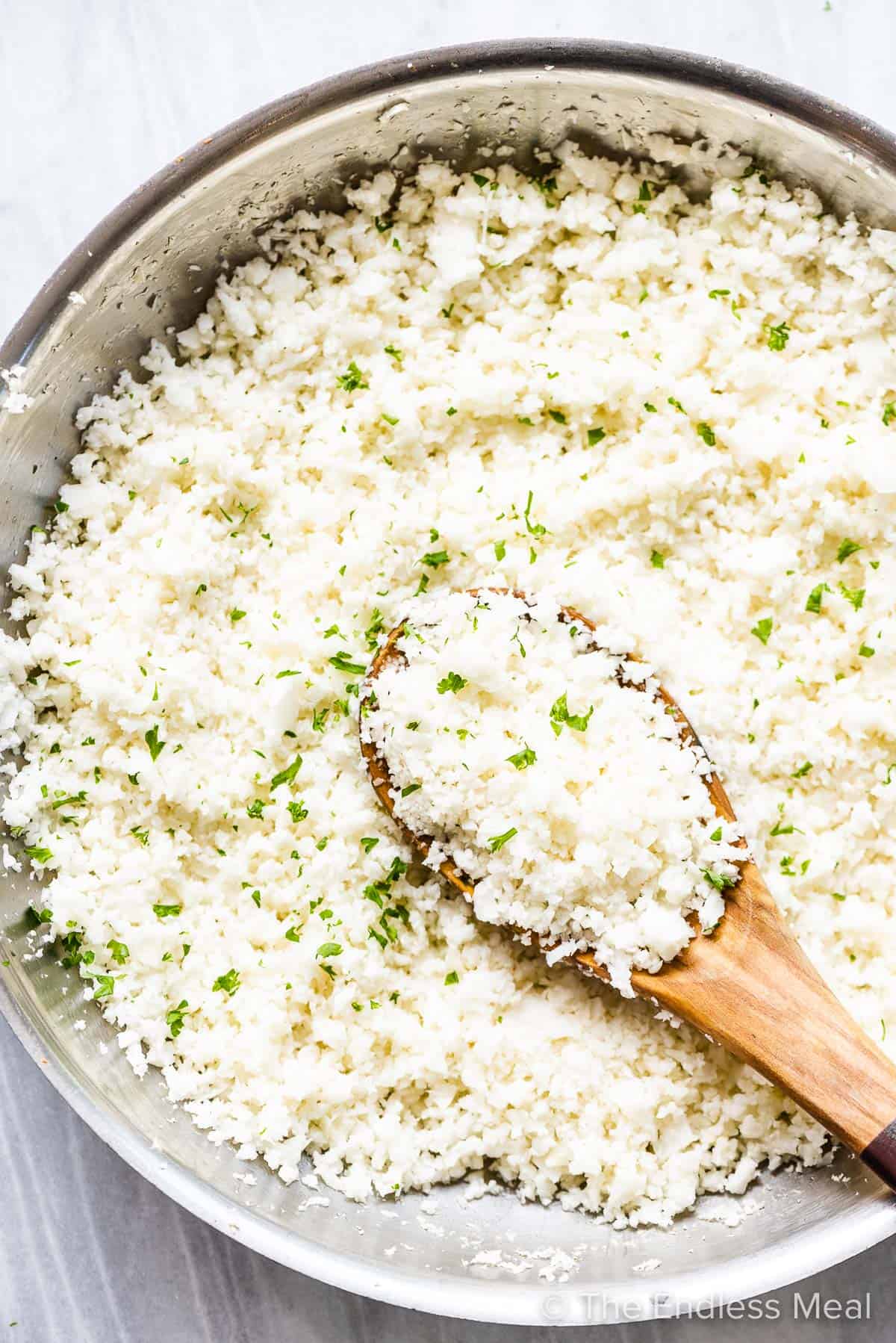 cauliflower rice in a pan with a wooden spoon.