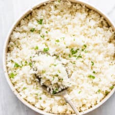 A white bowl with cauliflower rice and a spoon.