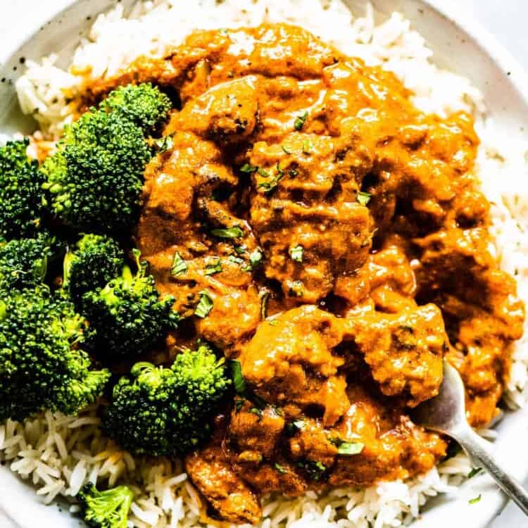 Chicken tikka masala on a plate with a side of rice and broccoli.