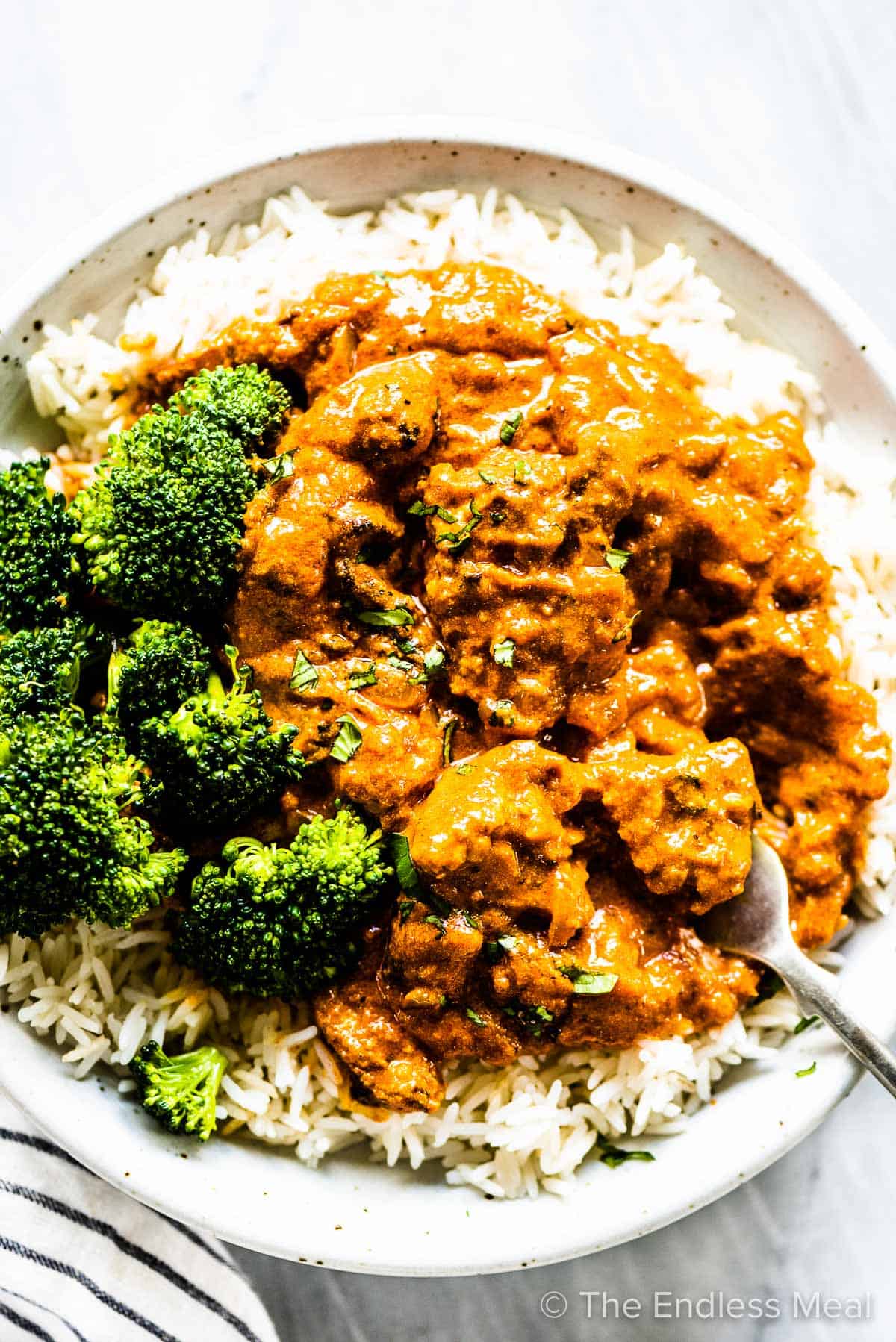 Chicken tikka masala on a plate with a side of rice and broccoli.