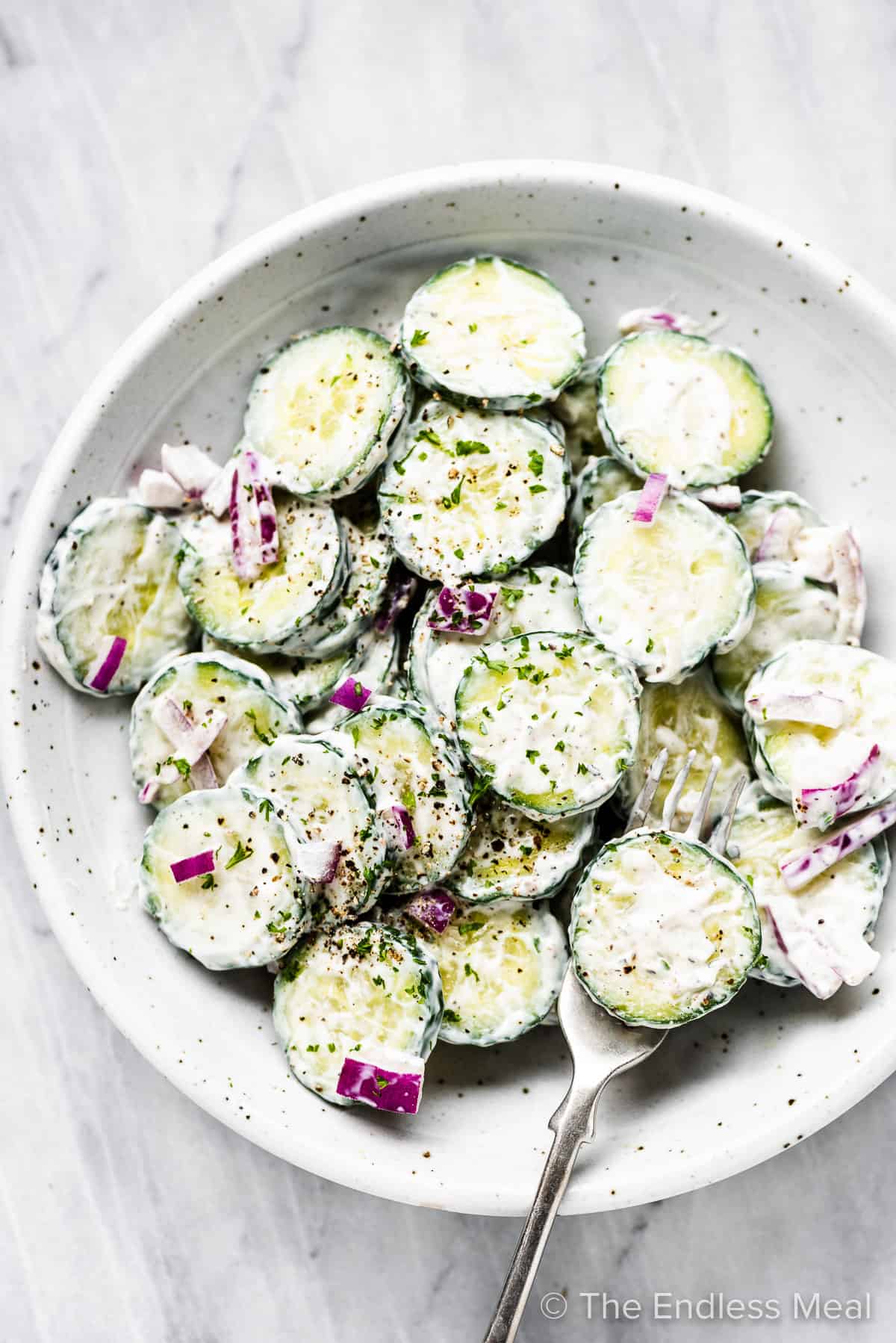 Creamy cucumber salad with red onion in a white bowl with a fork.