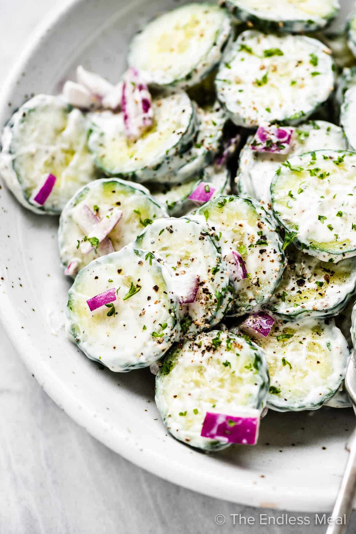 A close up of this creamy cucumber salad in a white serving bowl.