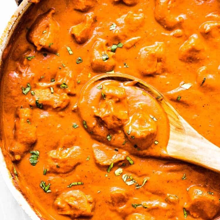 Butter chicken in a pan with a wooden spoon.