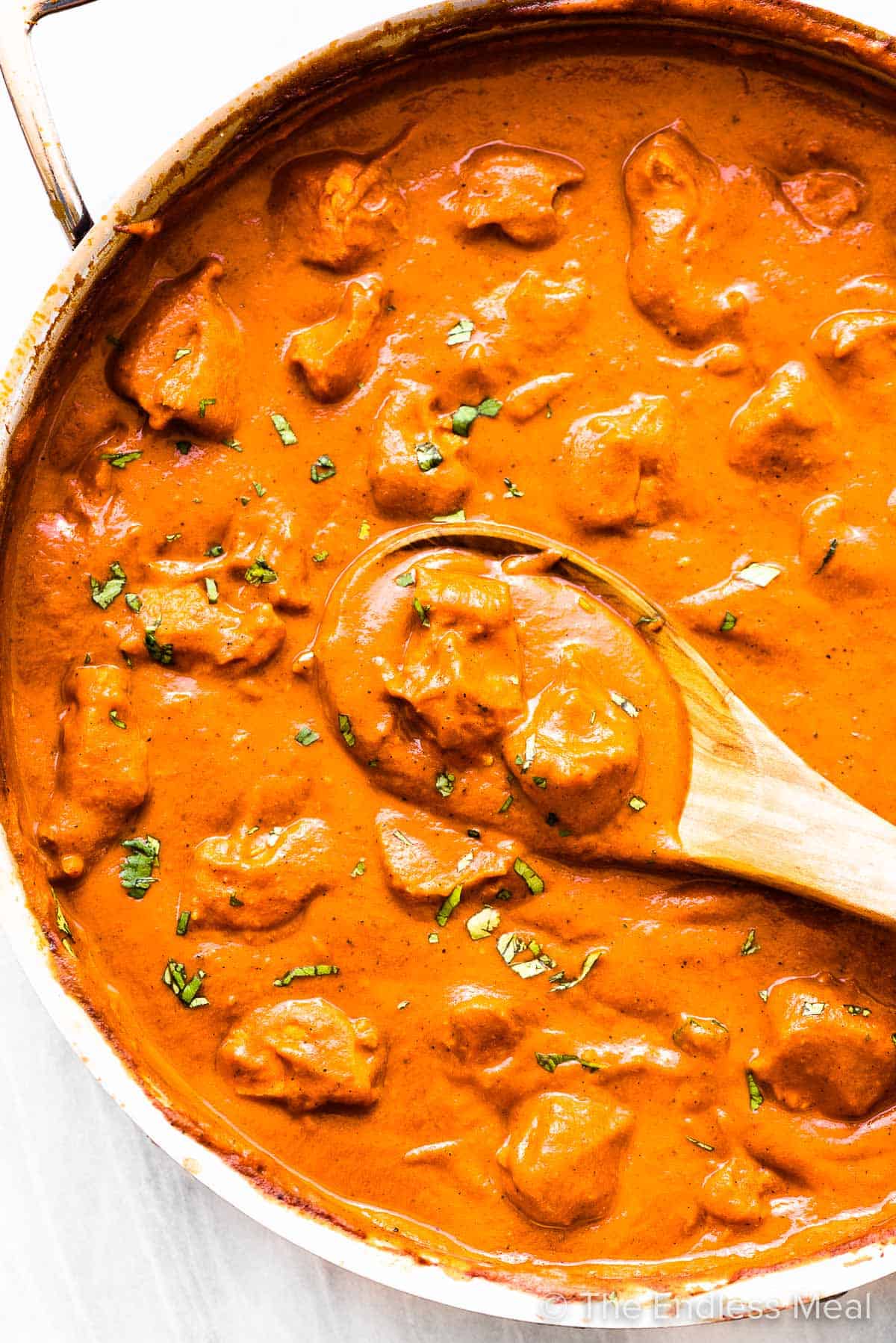 Butter chicken in a pan with a wooden spoon.