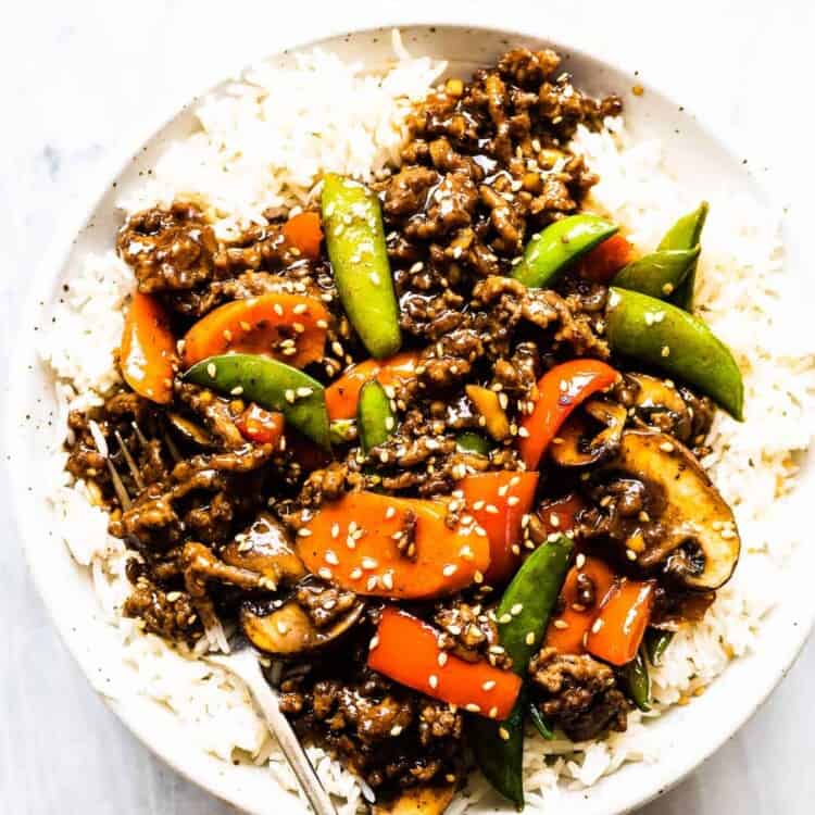 Ground beef stir fry on top of rice on a white plate.