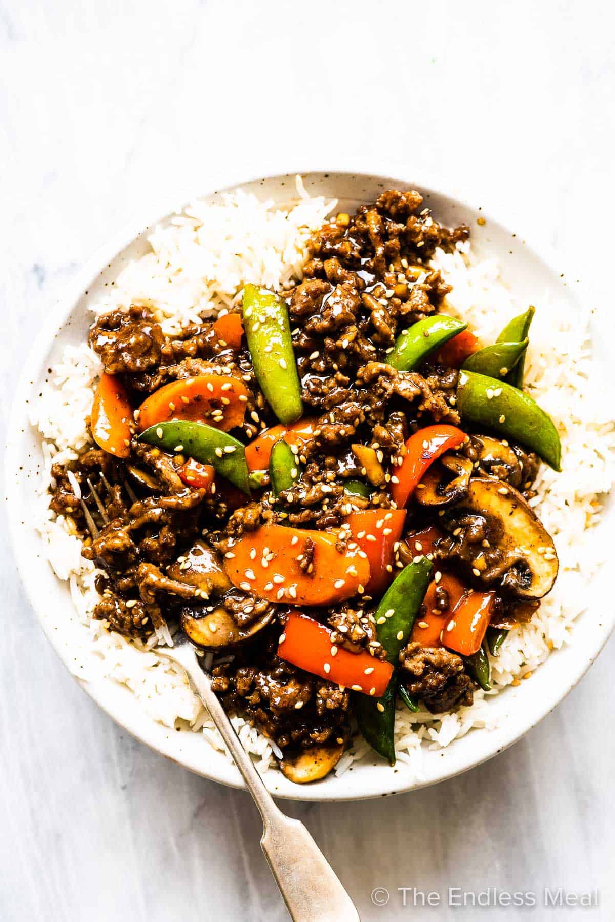 Ground beef stir fry on top of rice on a white plate. 