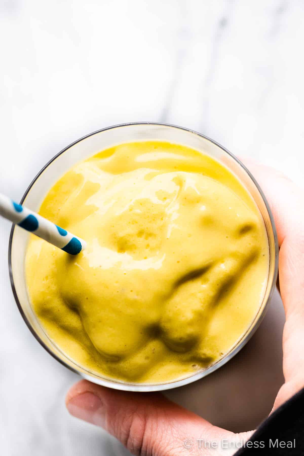 A hand holding a yellow smoothie.