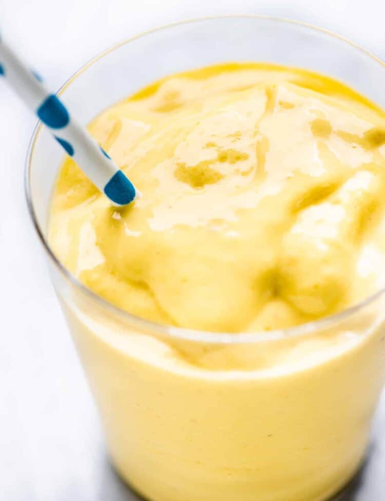 Mango smoothie in a glass with a straw.