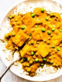 Mattar paneer over basmati rice on a white plate with a fork.