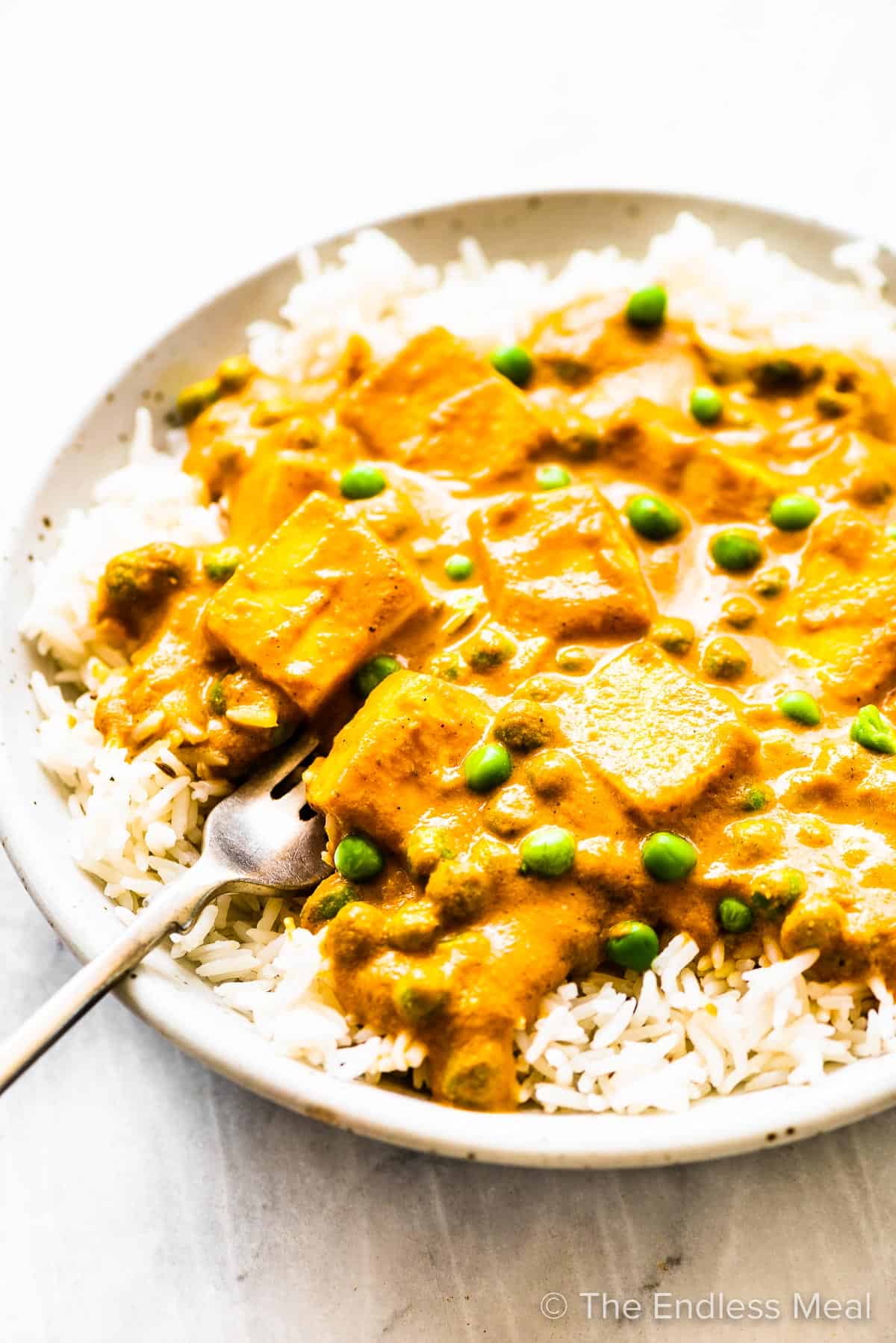 A fork taking a scoop of mattar paneer out of a bowl