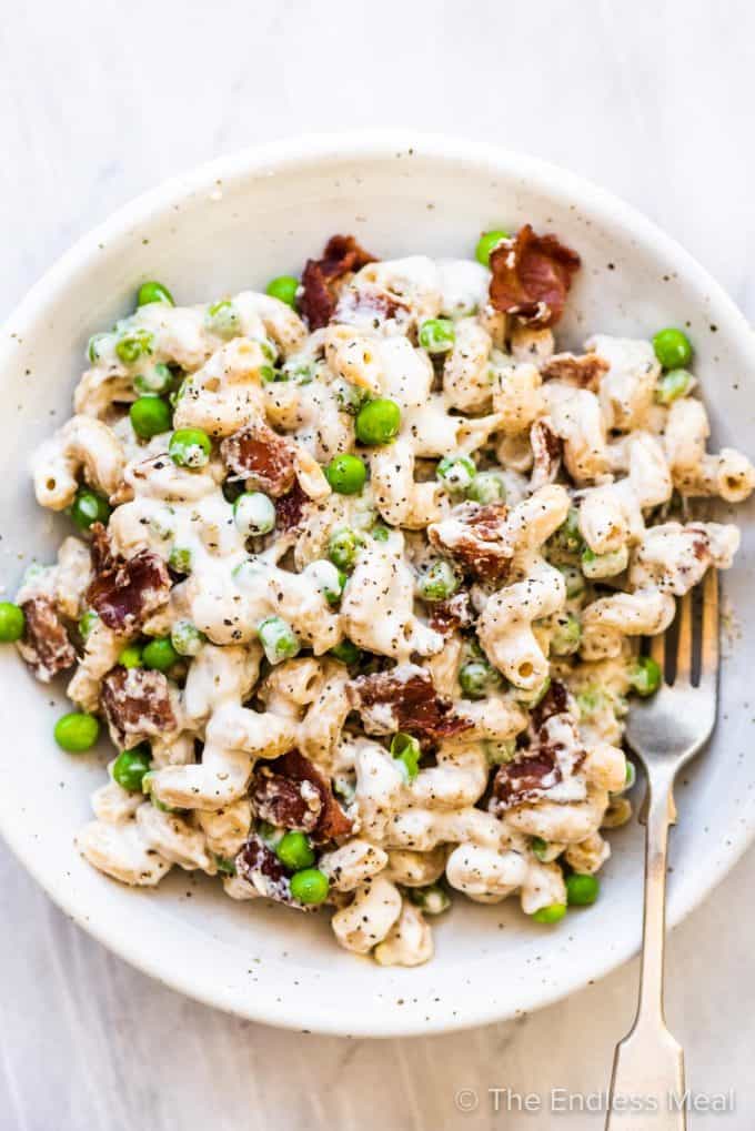 A white bowl filled with pasta with peas and bacon.