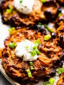 A close up of a sweet potato latke with sour cream on top.