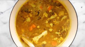 A pot of curried cauliflower soup with visible carrots simmering in a yellow broth on a marble countertop.
