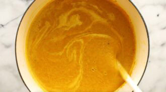 A pot of golden yellow curried cauliflower soup being stirred, showing a smooth, creamy texture with visible swirl patterns on the surface.