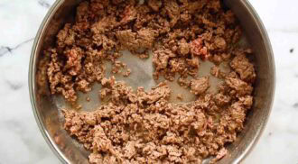 Cooked ground beef stir fry in a stainless steel pan on a marble countertop, with some pink areas indicating it’s partially browned.