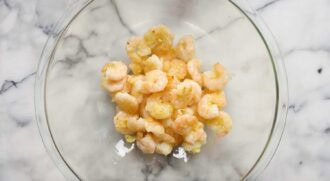A glass bowl containing cooked, seasoned honey walnut shrimp on a white marble surface.