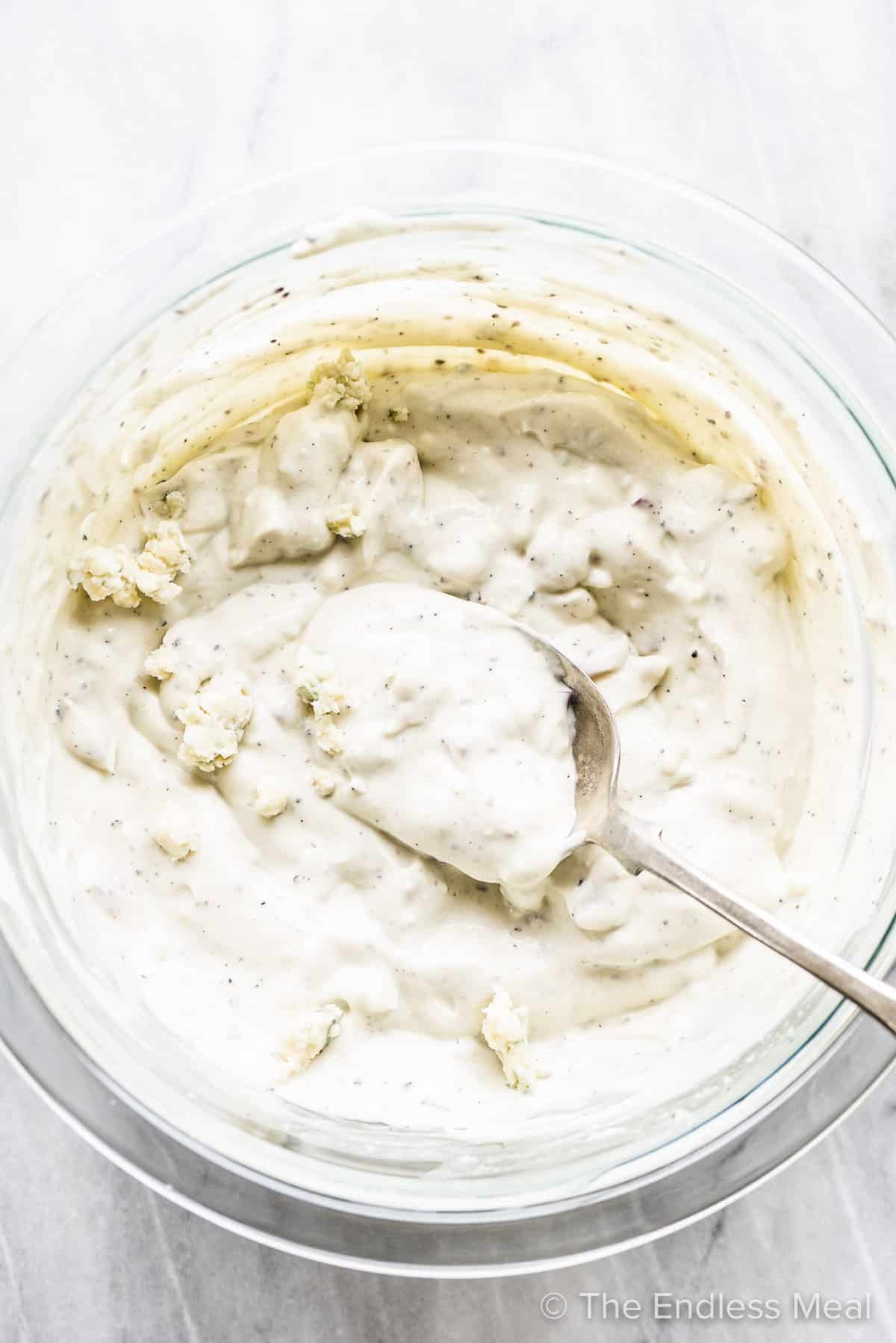 Blue cheese dressing in a glass bowl with a spoon.