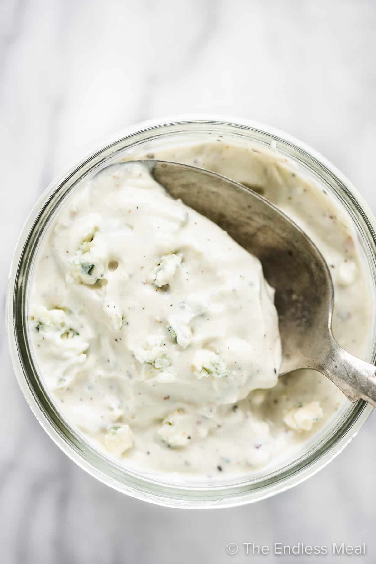 Blue cheese dressing in a jar with a spoon taking a scoop.
