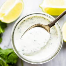 Cilantro lime ranch dressing in a glass jar with a spoon and limes and cilantro around the jar.