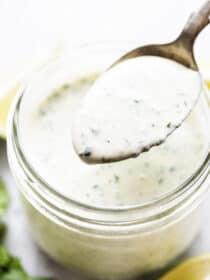 A spoon taking a scoop of cilantro lime ranch dressing out of a glass jar.