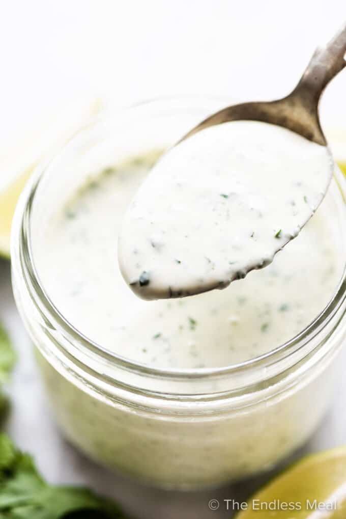 A spoon taking a scoop of cilantro lime ranch dressing out of a glass jar.