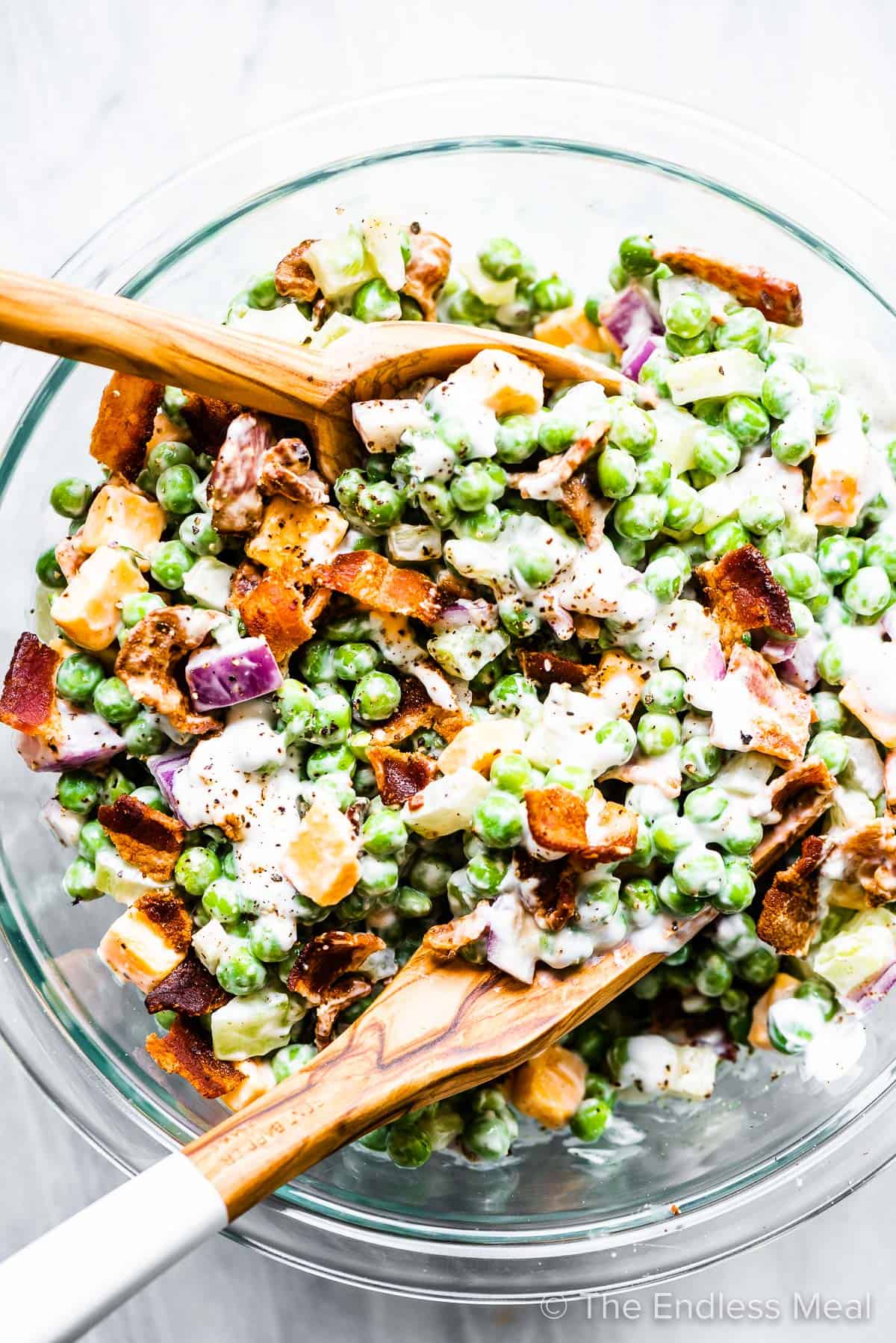 Serving pea salad with bacon, cheese, and onion.