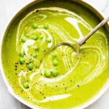Pea soup in a bowl with some fresh peas on top.