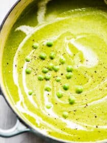 A close up of pea soup in a pot with thawed frozen peas on top.