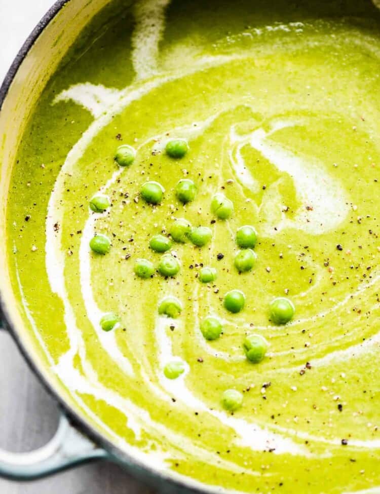A close up of pea soup in a pot with thawed frozen peas on top.