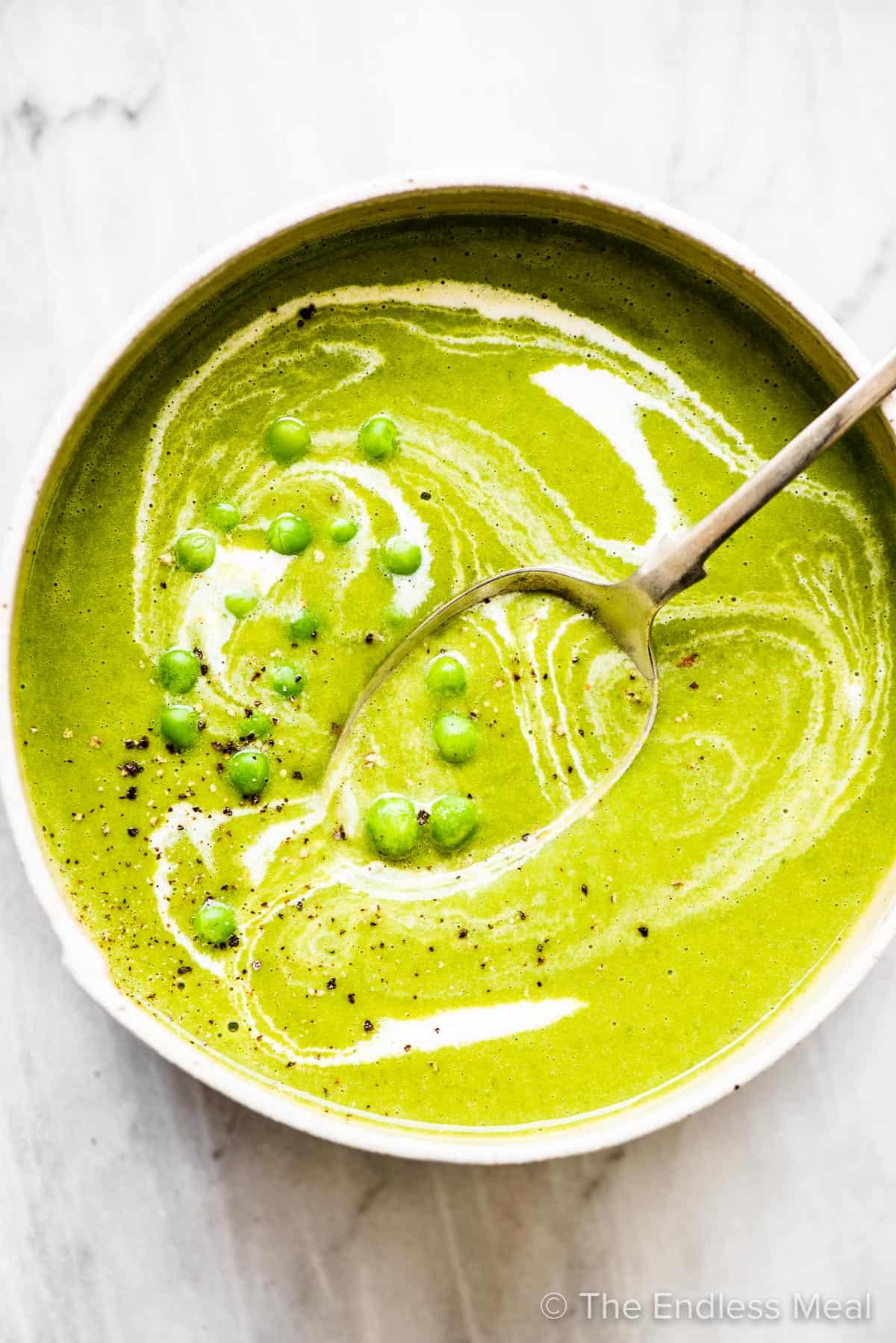 Pea soup in a bowl with some fresh peas on top.