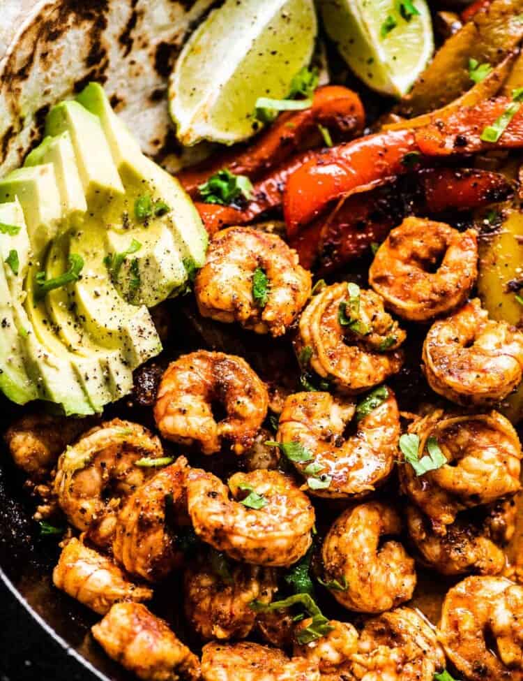 A close up of shrimp fajitas in a pan with avocado and limes.