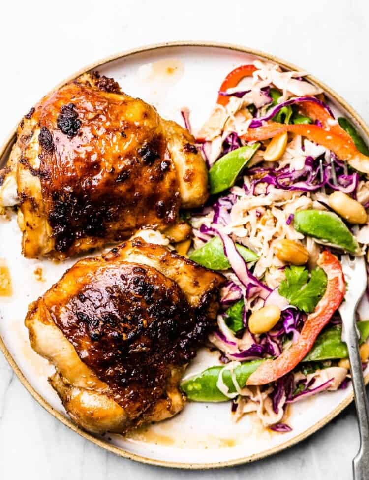 A white plate with 2 garlic ginger chicken thighs and coleslaw.