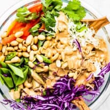 Peanut coleslaw in a glass bowl with wooden salad tongs.