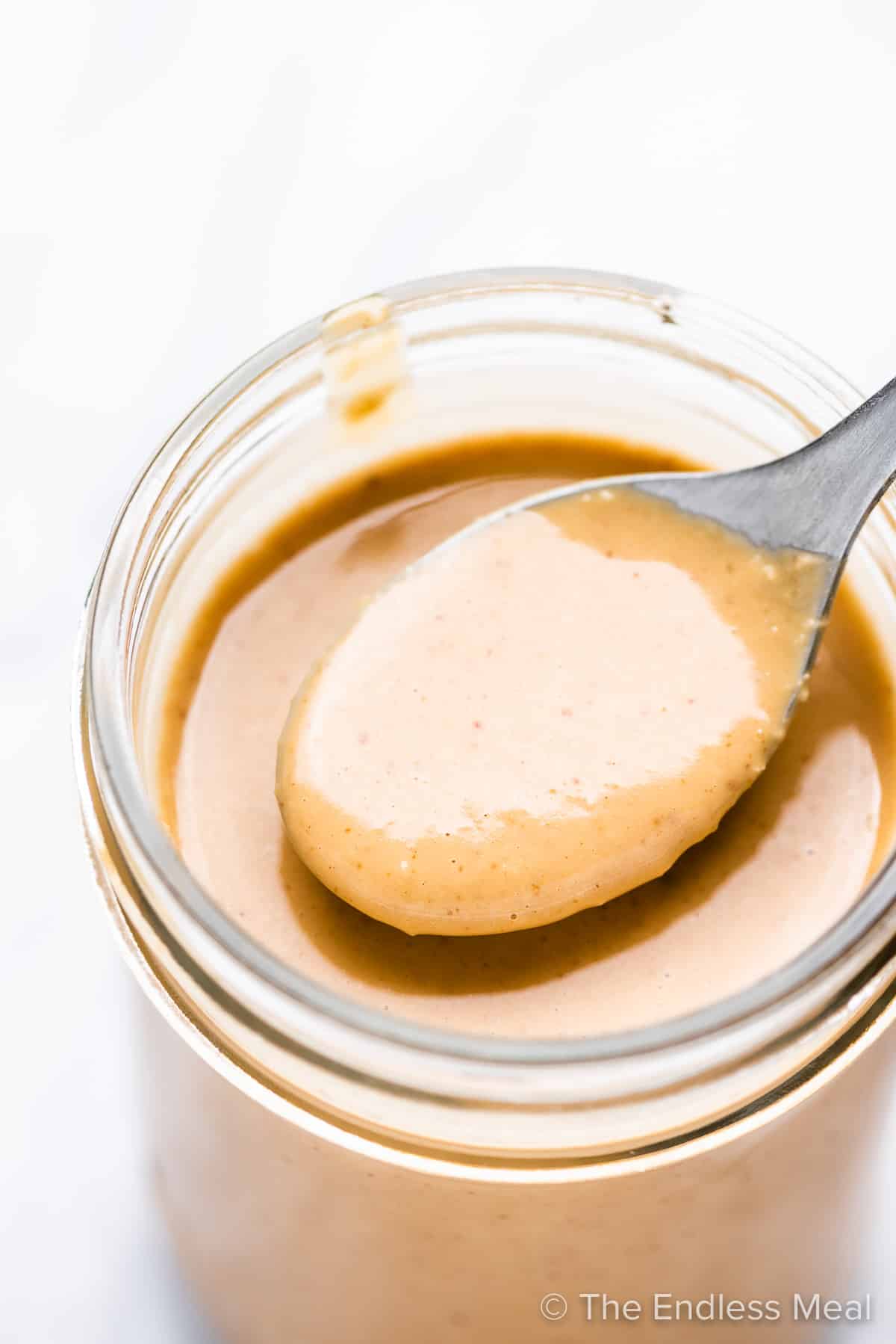 A spoon taking some peanut dressing out of a glass jar.