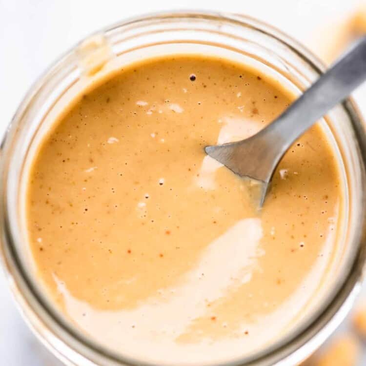 a glass jar filled with peanut salad dressing an a spoon inside.