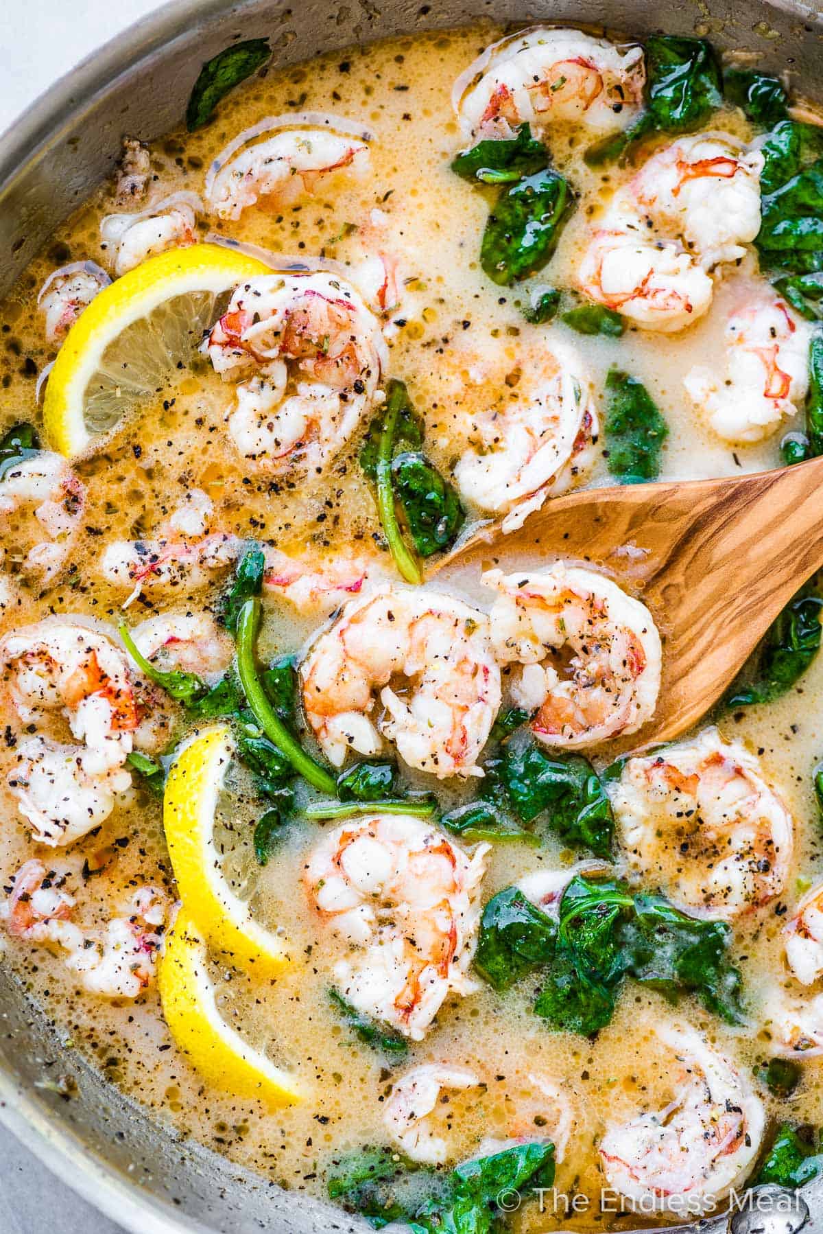 Lemony shrimp scampi in a pan with a wooden spoon.