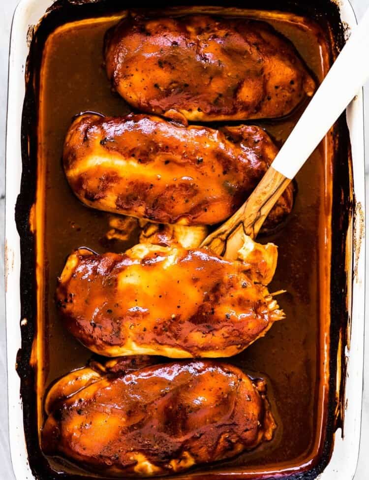 Four cooked chicken breasts covered with bbq sauce in a baking dish.