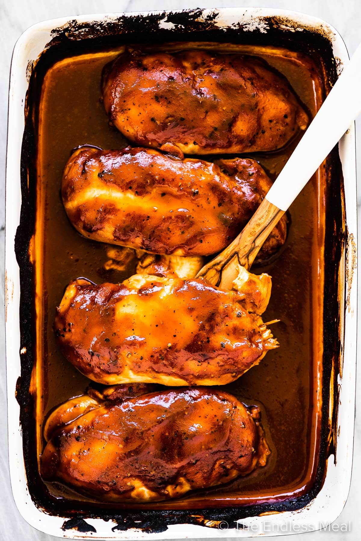 Four cooked chicken breasts covered with bbq sauce in a baking dish.