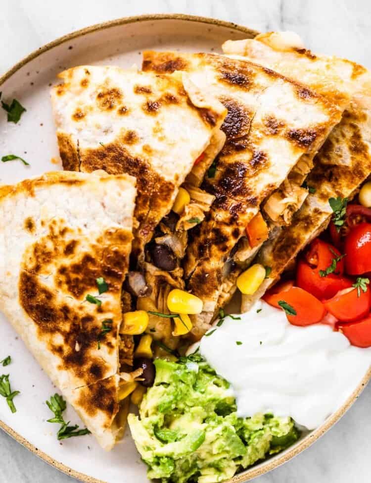 A bbq chicken quesadilla on a white plate with sour cream, guacamole, and salsa on the side.