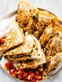 A plate piled high with bbq chicken quesadillas with salsa and sour cream on the side.