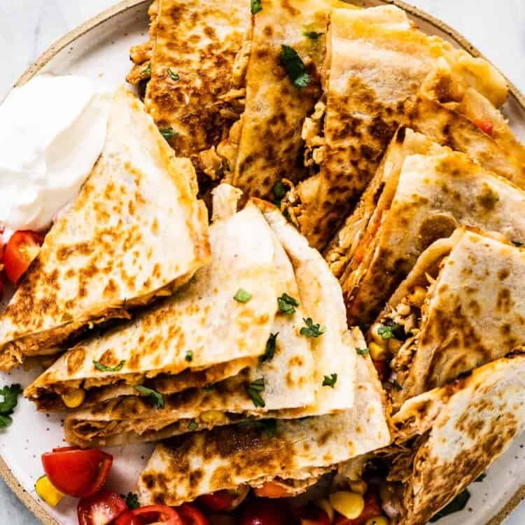 A plate piled high with bbq chicken quesadillas with salsa and sour cream on the side.
