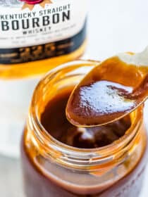 A jar of bourbon bbq sauce with a bottle of bourbon in the background.
