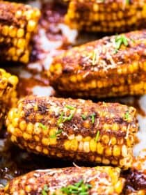 Parmesan corn on the cob on a baking sheet with some green onions on top.