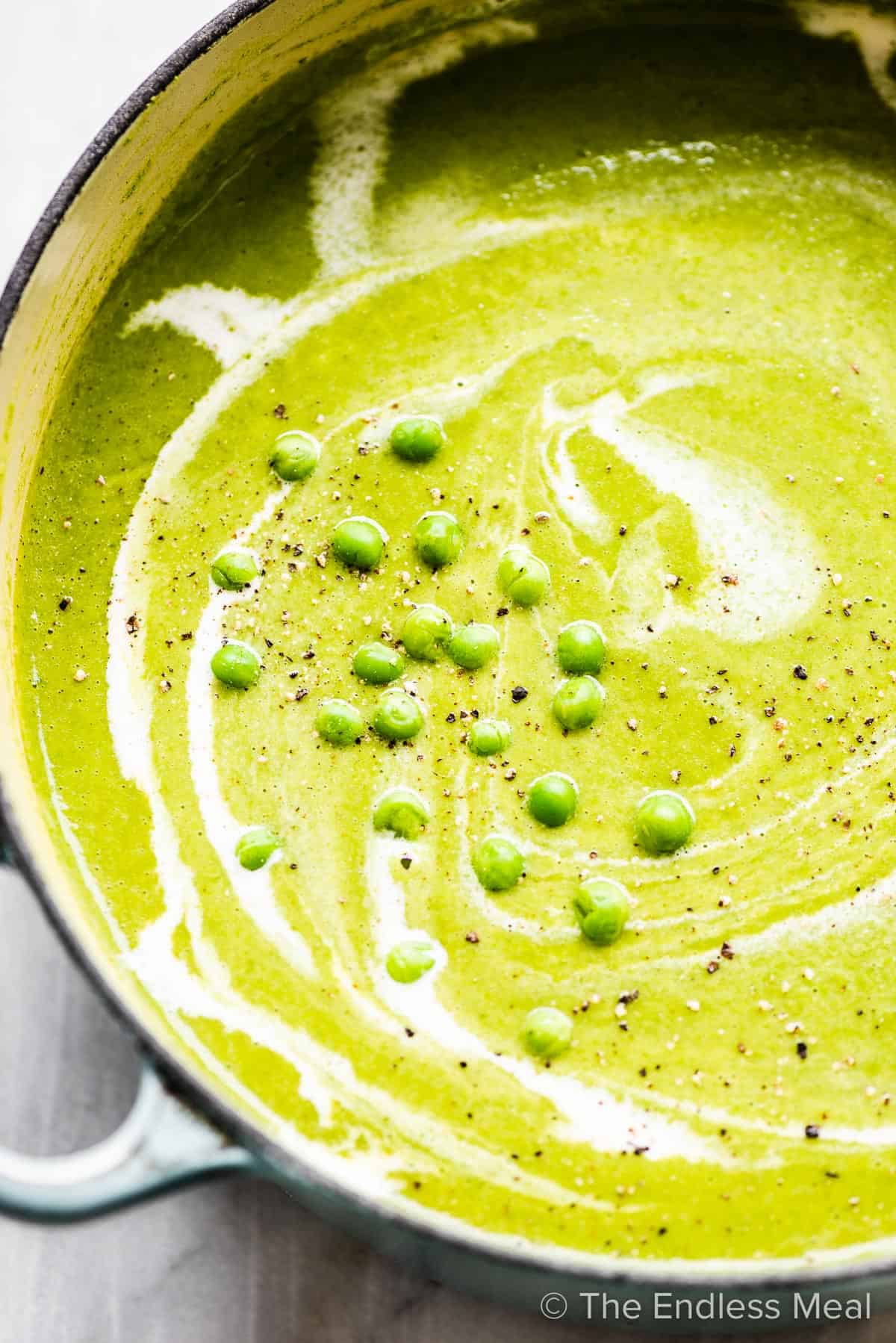 A photo of a cast iron pot filled with creamy green pea soup, swirled with white yogurt, and topped with fresh peas.