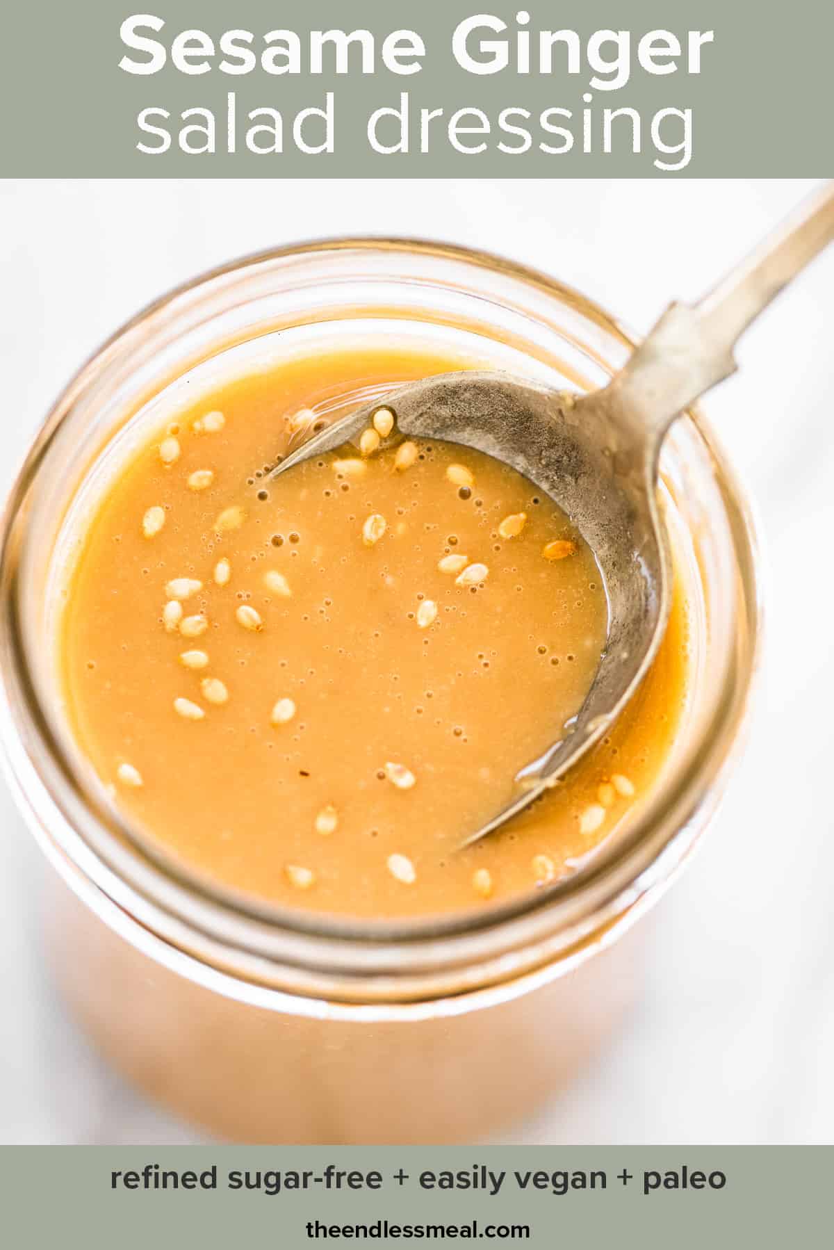 Sesame ginger dressing in a glass jar with a spoon in it and the recipe title on top of the picture.