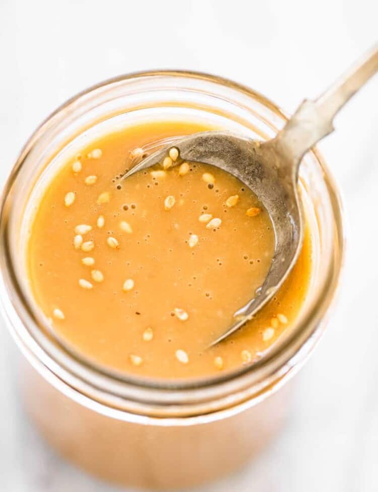 Sesame ginger dressing in a glass jar with a spoon in it.